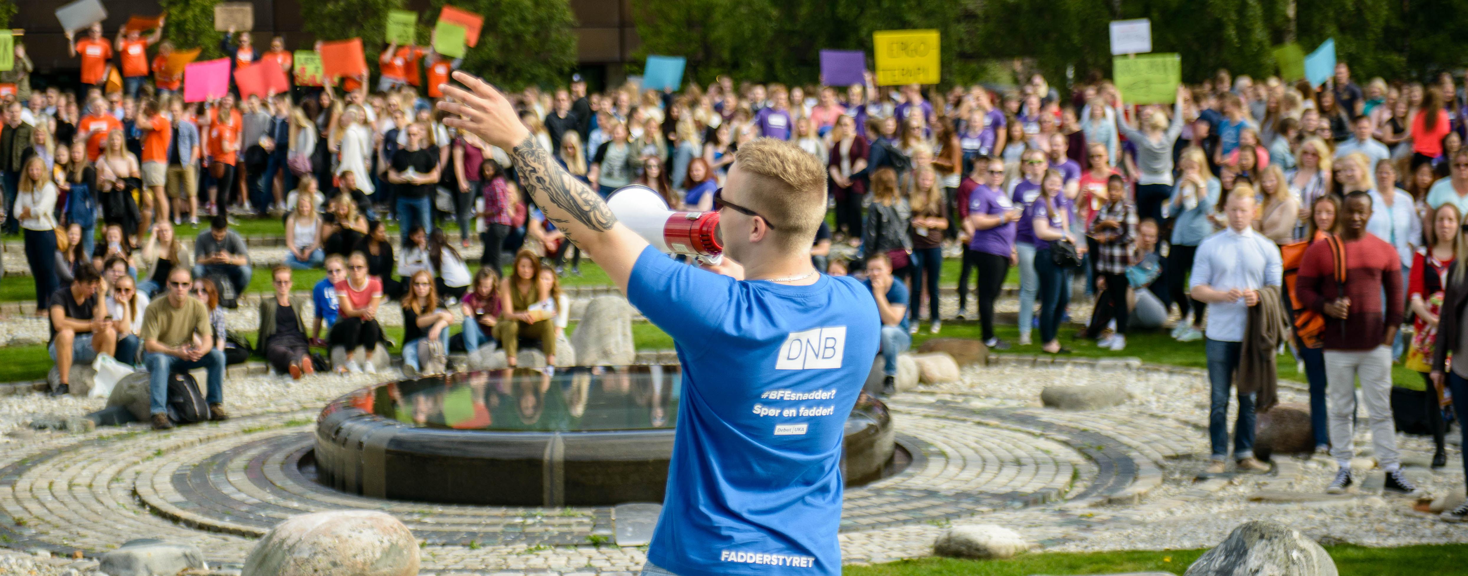 Student fadder med ropert foran hundevis av studenter