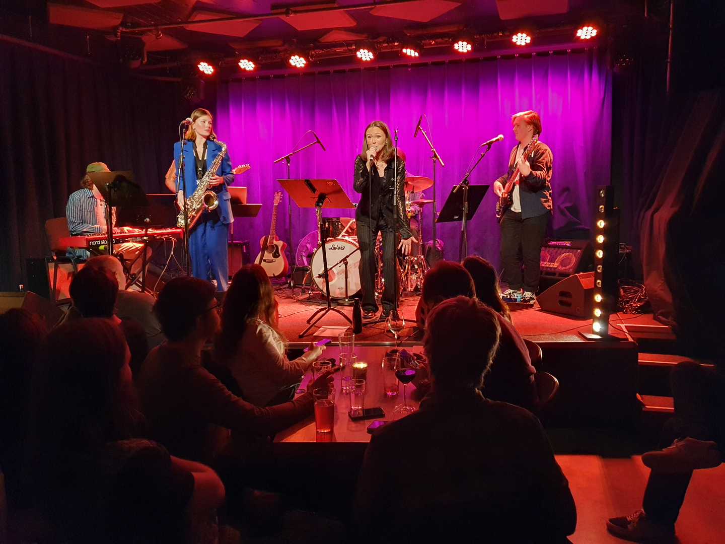 UiT_Nach_pa_Bakrommet_UIT_24449_Foto_Jorn_Berger_Nyvoll.jpg Et band spiller i et lokale med mye lilla og rødt lys.