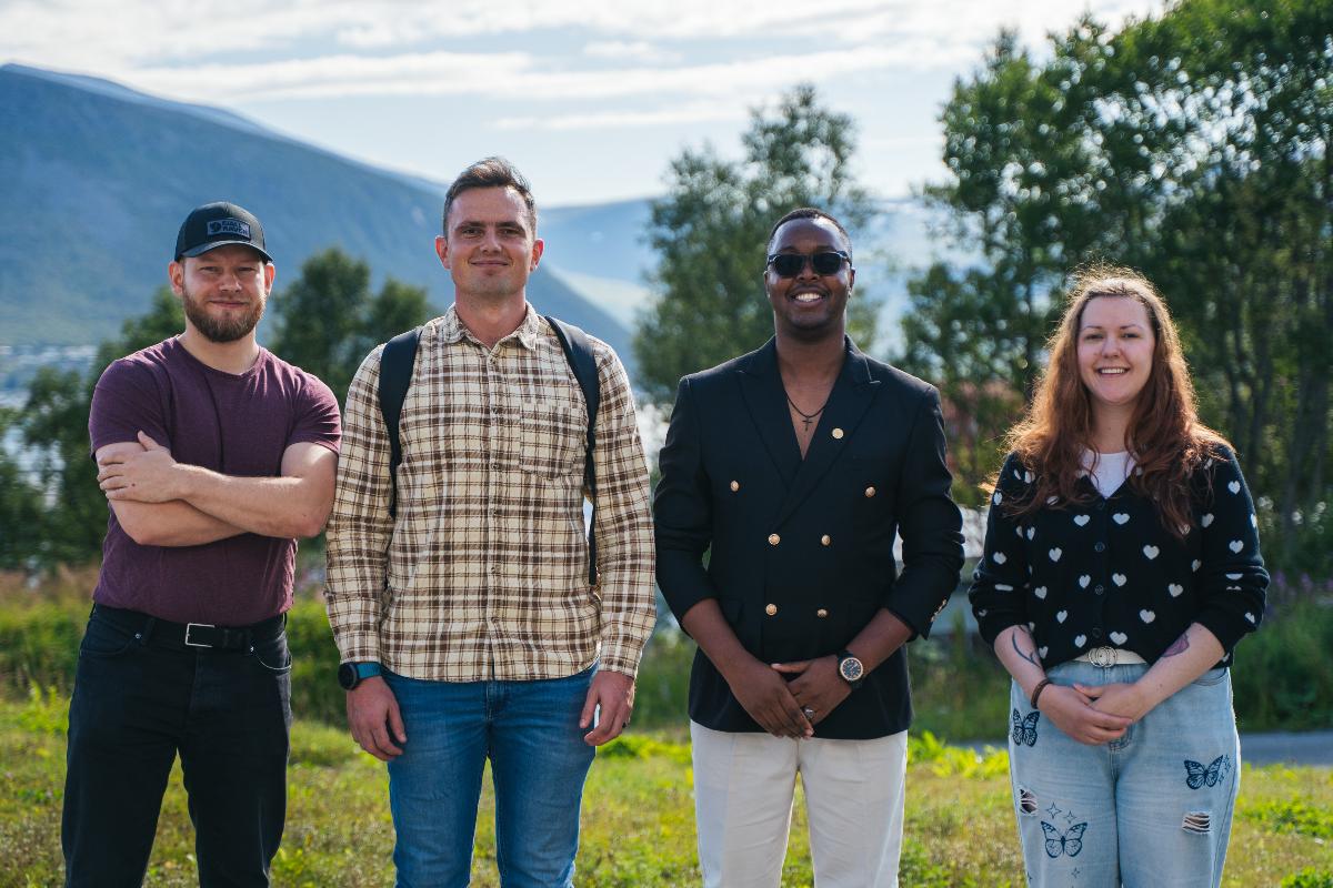 Fire studenter, tre gutter og ei jente smler mot kamera. De st&aring;r ute og det er sommer