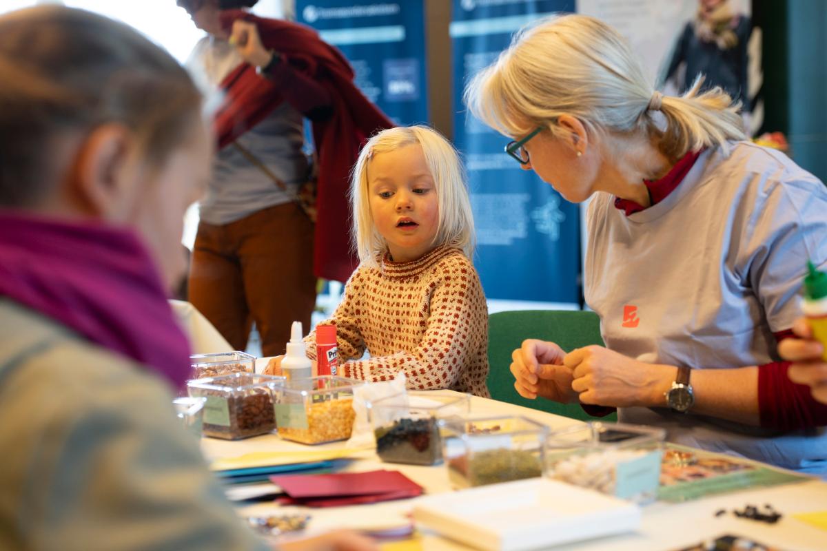 barn med lyst hår som sitter og gjør en hobbyaktivitet sammen med en dame