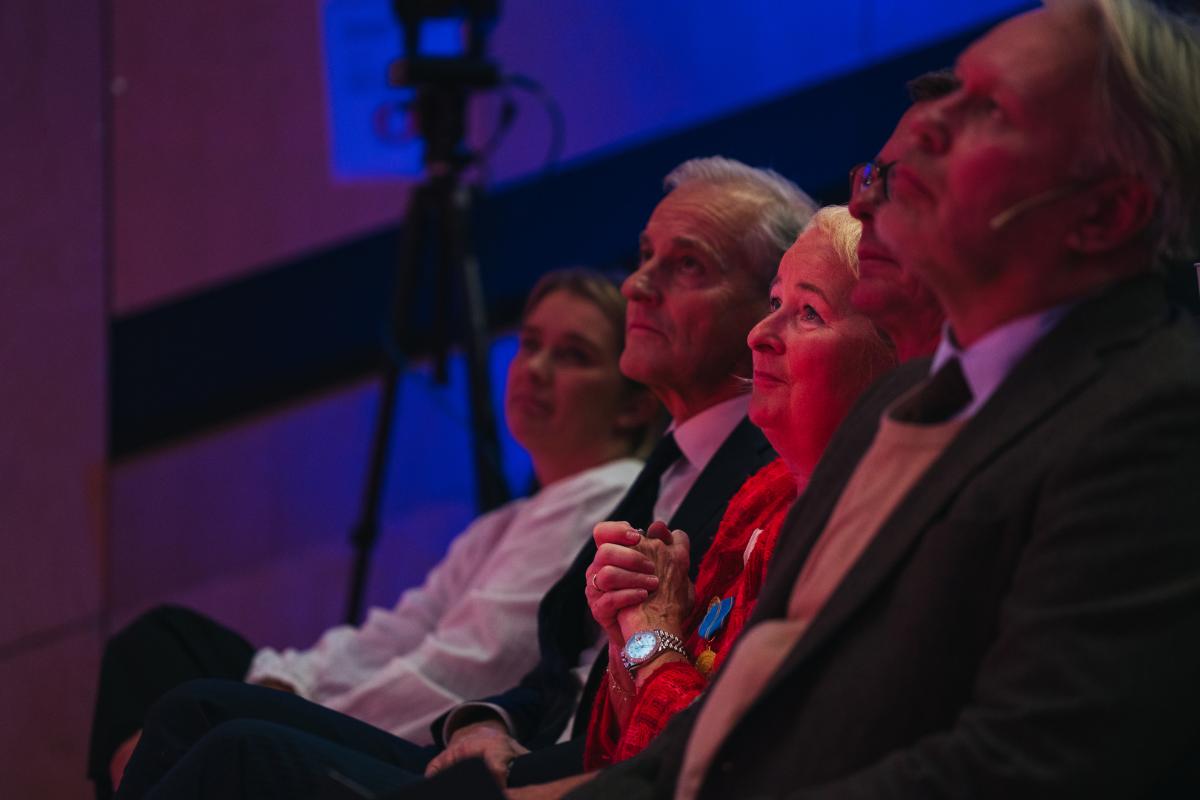 Ei rekkje med menneskje sit fremst i eit auditorium og lyttar.