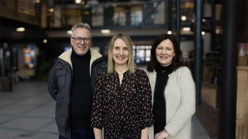 De tre artikkelforfatterne st&aring;r i foajeen ved UiT i Harstad og ser inn i kamera