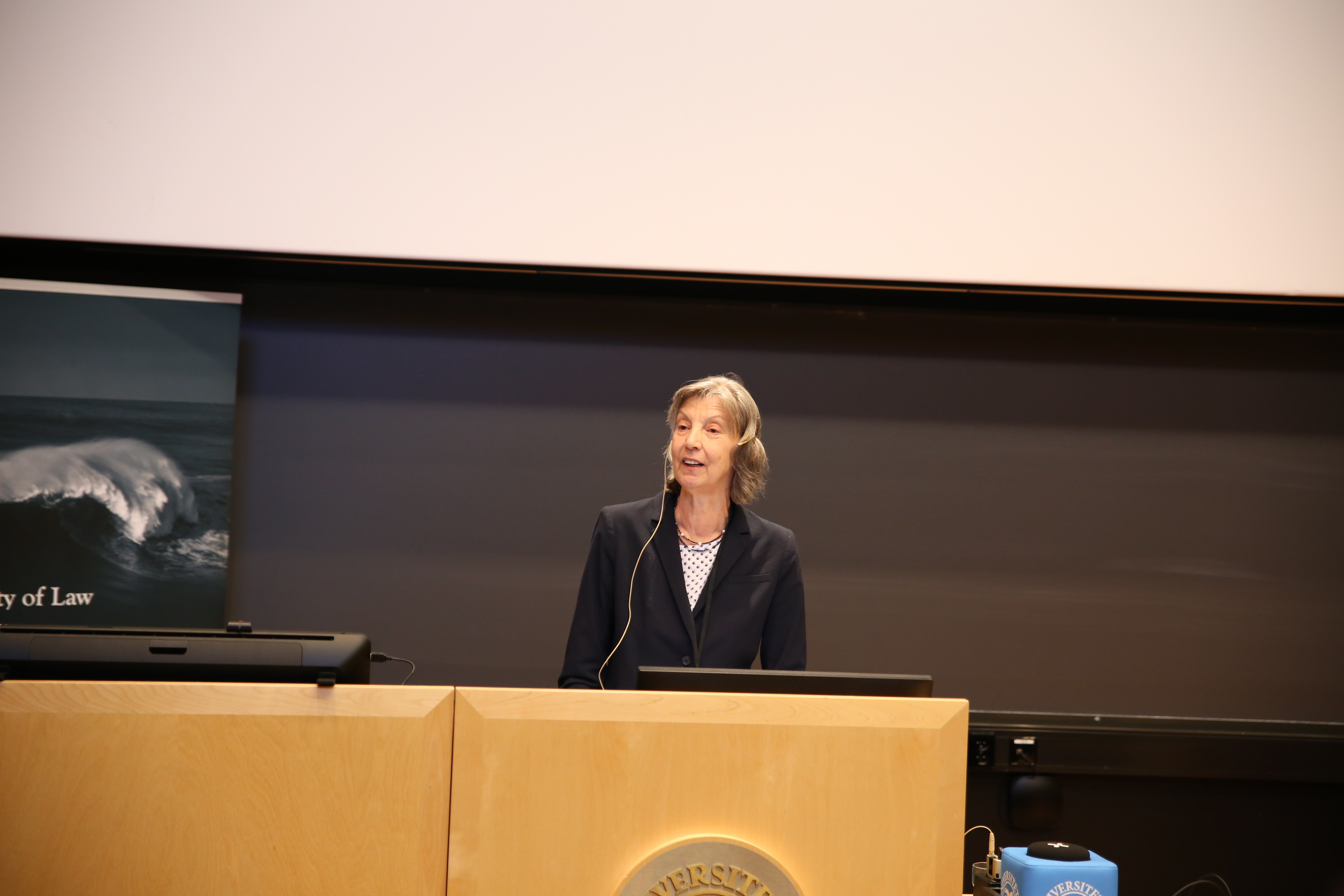 woman standing in front of a podium, seaking to an audience.