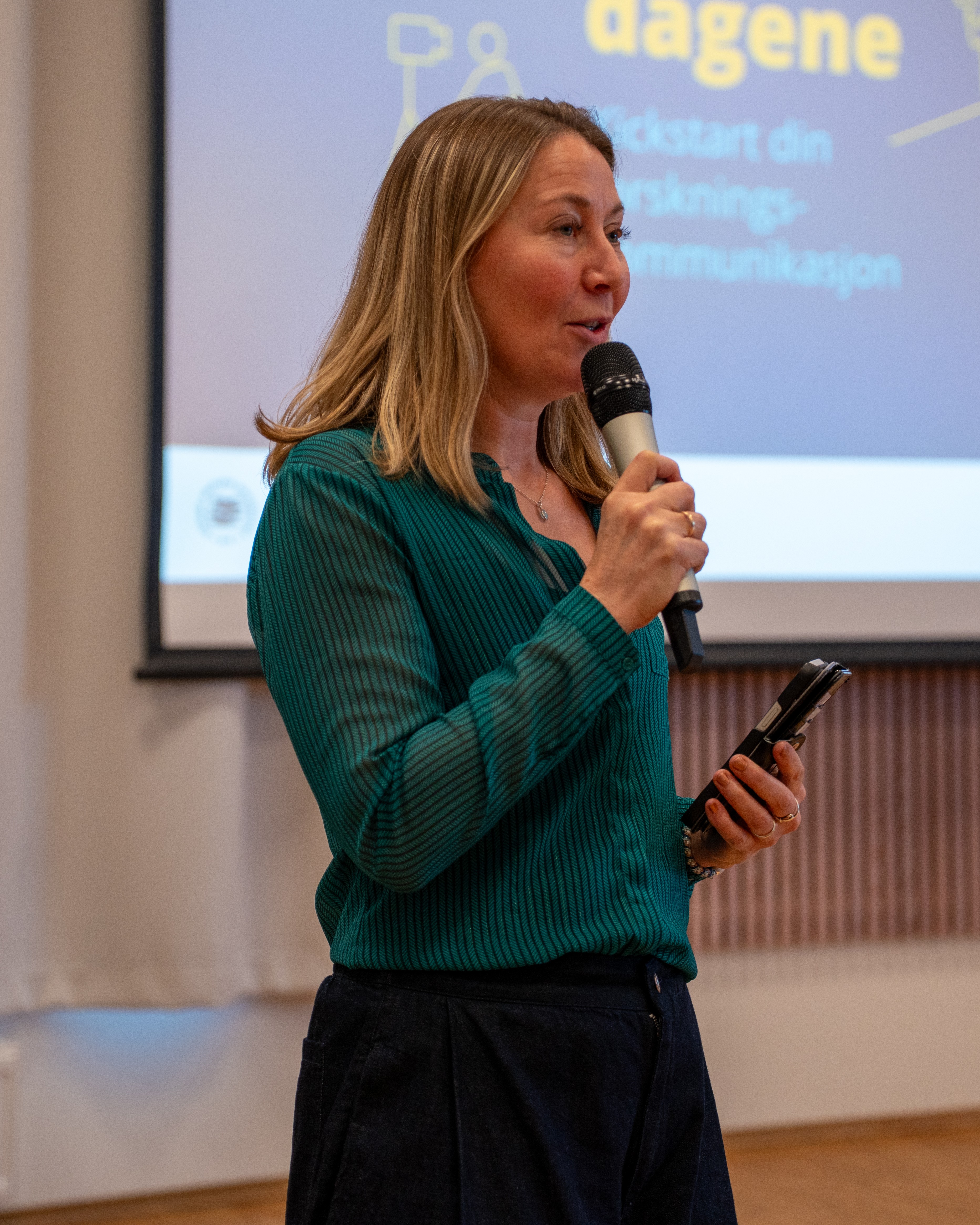 Kvinne som holder en mikrofon med storskjerm i bakgrunnen.