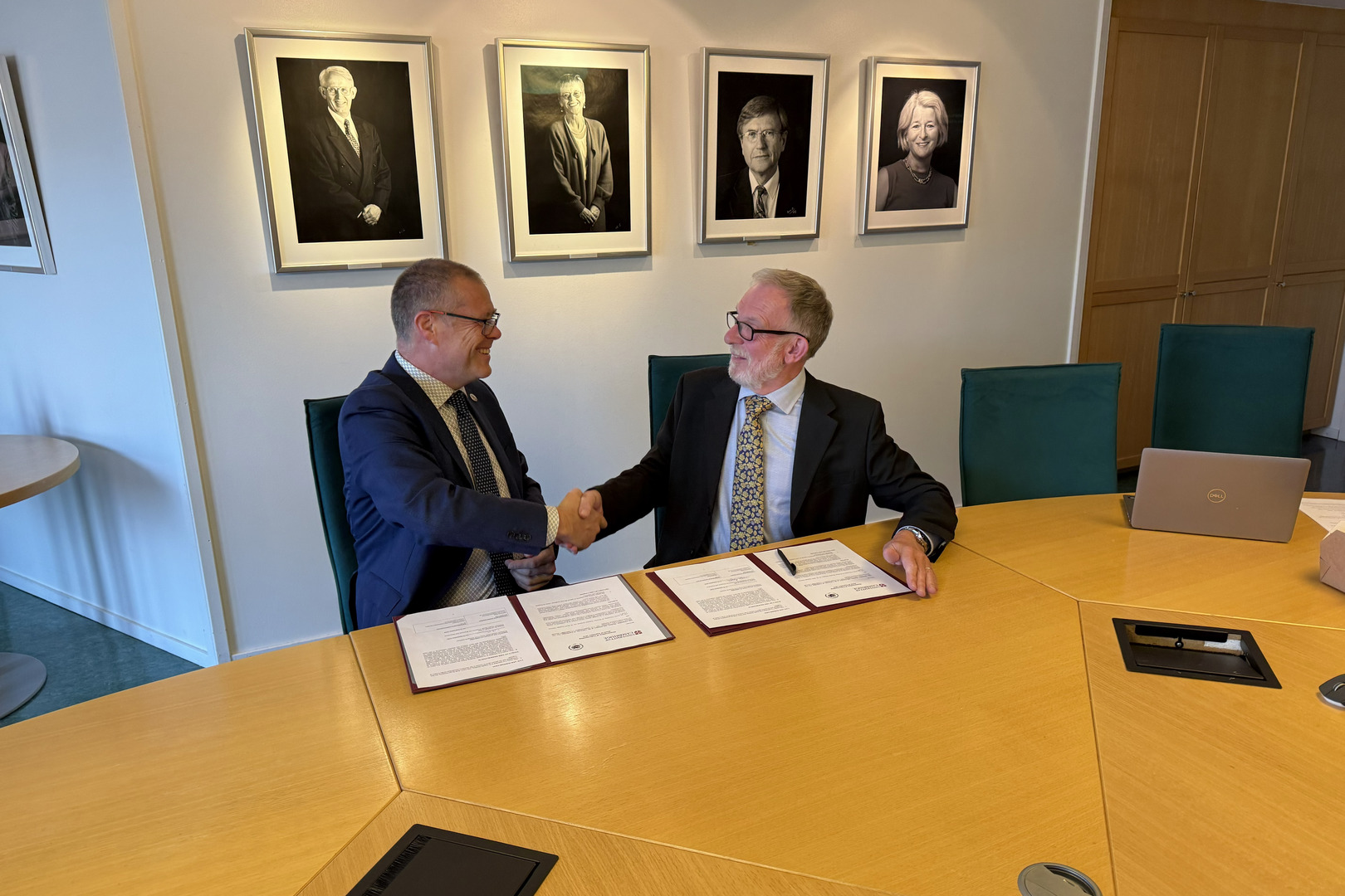 Dette1.jpg To personer ved et bord som gir hverandre et håndtrykk.